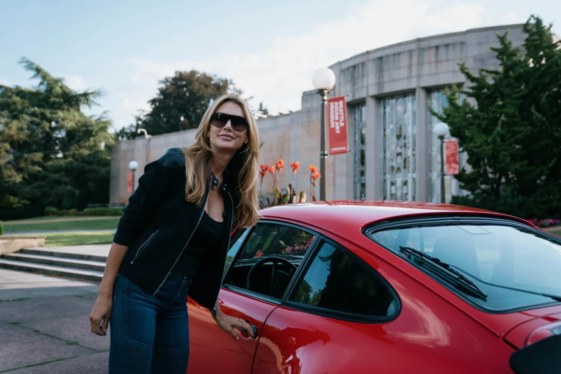 A woman standing next to a red car.