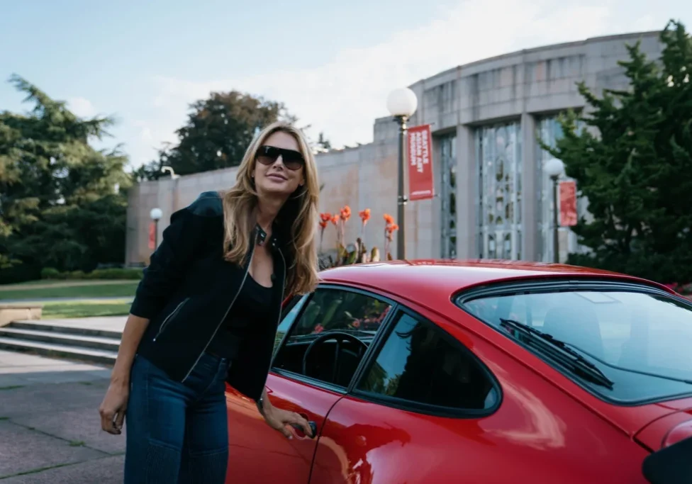 A woman standing next to a red car.